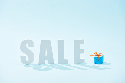 white sale lettering and festive gift box on blue background