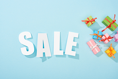 top view of white sale lettering and festive gift boxes on blue background