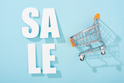 top view of white sale lettering and decorative shopping cart on blue background