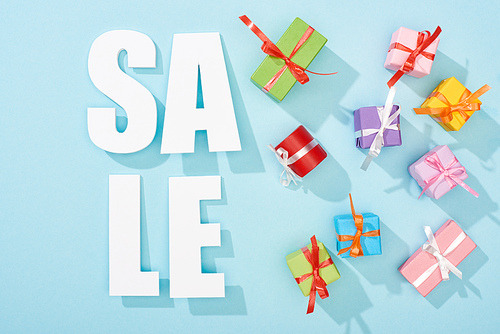 top view of white sale lettering and festive wrapped presents on blue background
