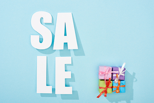 top view of white sale lettering near festive gift boxes on blue background
