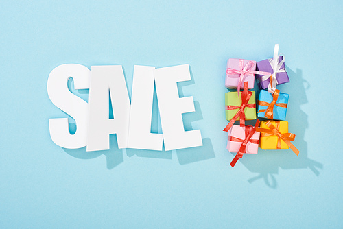 top view of white sale lettering and festive colorful gift boxes on blue background