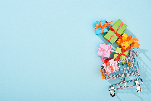 top view of colorful festive gift boxes in shopping cart on blue background