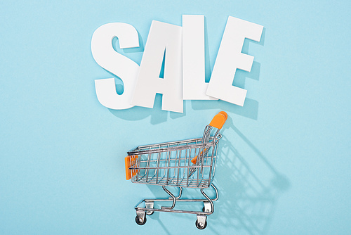 top view of white sale lettering and empty shopping cart on blue background