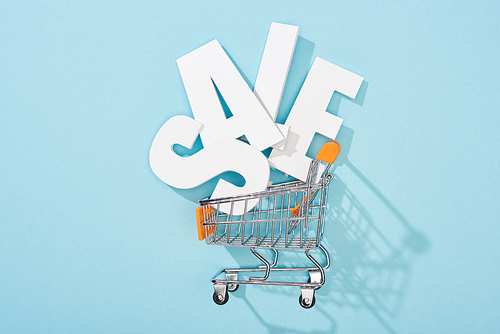 top view of white sale lettering in decorative shopping cart on blue background