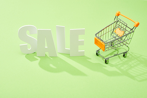 white sale lettering near decorative shopping cart on green background