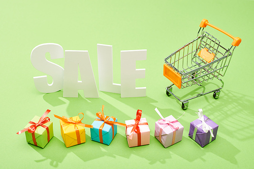 white sale lettering near decorative gift boxes and shopping cart on green background