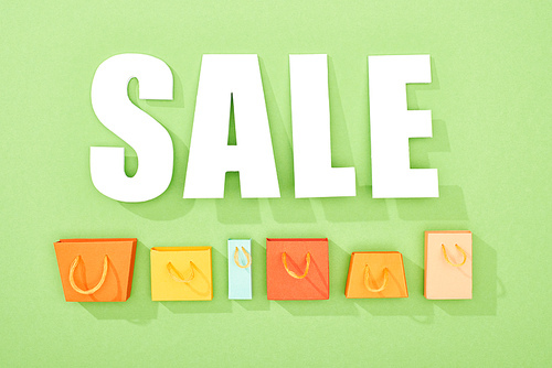 top view of decorative shopping bags and white sale lettering on green background
