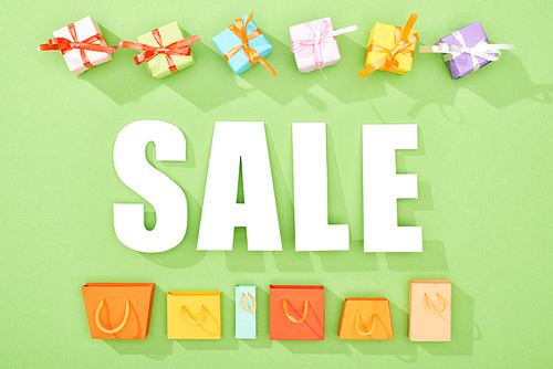top view of decorative gift boxes and shopping bags on green background with sale lettering