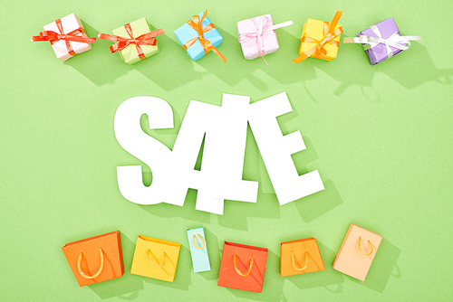 top view of decorative gift boxes and shopping bags on green background with sale word