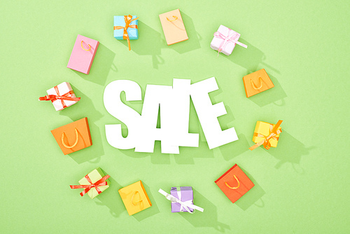 round frame of decorative gift boxes and shopping bags on green background with sale lettering