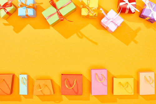 top view of festive wrapped gifts and shopping bags on bright orange background