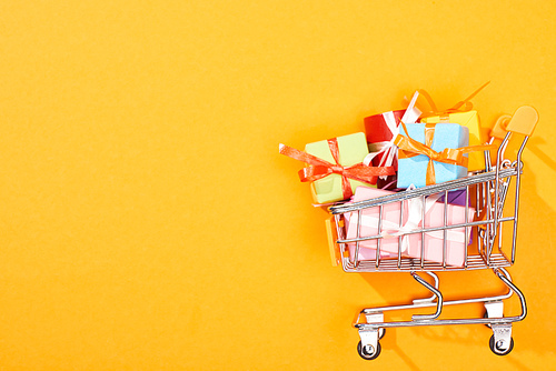 top view of shopping cart with presents on bright orange background