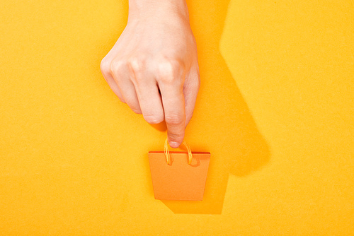 cropped view of hand holding small shopping bag on bright orange background