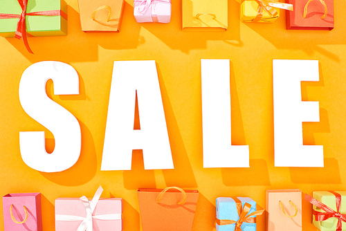 top view of white sale lettering near shopping bags and presents on bright orange background
