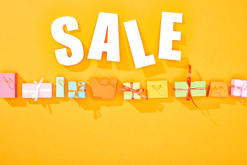 top view of white sale lettering above shopping bags and gifts on bright orange background with copy space