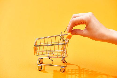 cropped view of woman pushing small shopping cart on bright orange background