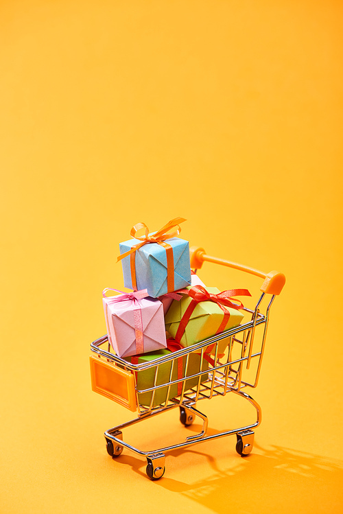 decorative shopping trolley with presents on bright orange background