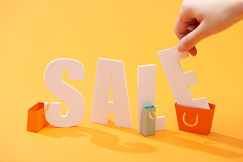 cropped view of man holding letter from white sale lettering near shopping bags on orange background