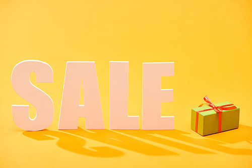 white sale lettering near wrapped gift box on bright orange background