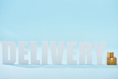 white delivery word near closed cardboard boxes on blue background with copy space