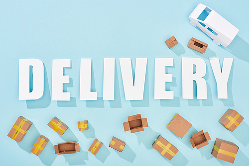 top view of delivery lettering with shadows near cardboard boxes and van on blue background