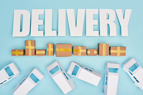 delivery inscription near closed cardboard boxes and mini vans on blue background