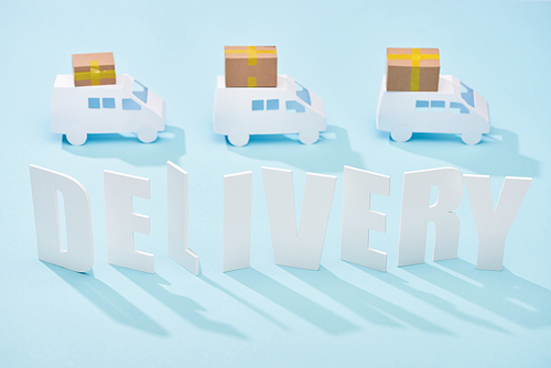 white delivery inscription under mini trucks with cardboard boxes on blue background