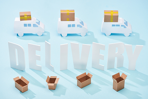 white delivery inscription between mini trucks and open cardboard boxes on blue background