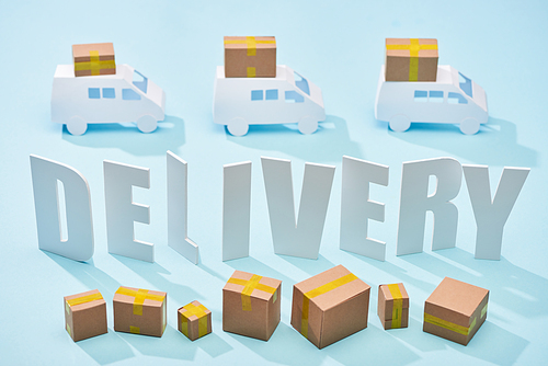white delivery inscription between mini trucks and closed cardboard boxes on blue background
