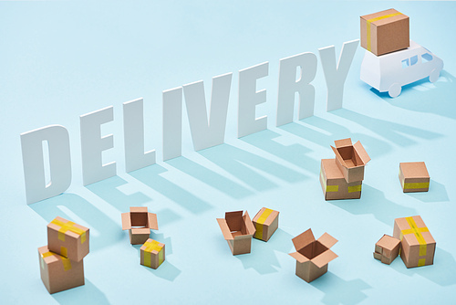 white delivery inscription near mini truck with cardboard boxes on blue background