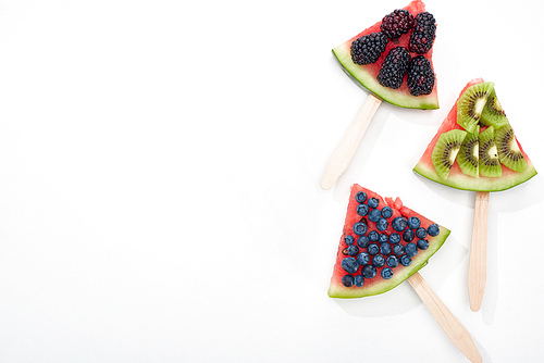 top view of delicious watermelon on sticks with seasonal berries and kiwi on white background with copy space