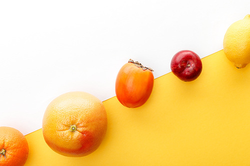 Top view of orange, grapefruit, lemon, persimmon and apple on yellow and white background