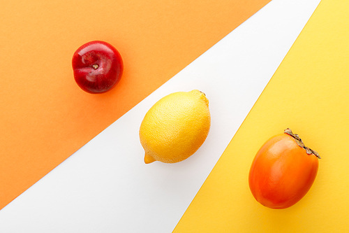 Top view of lemon, persimmon and apple on yellow, orange and white background