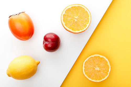 Top view of orange halves, persimmon, lemon and apple on yellow and white background