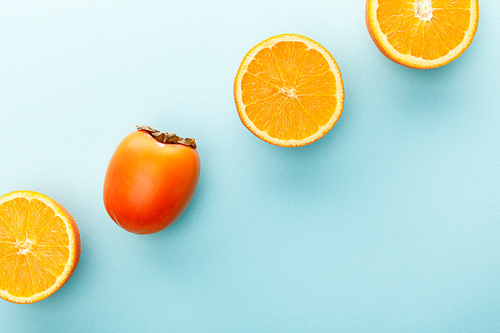 Top view of oranges halves and persimmon on blue background