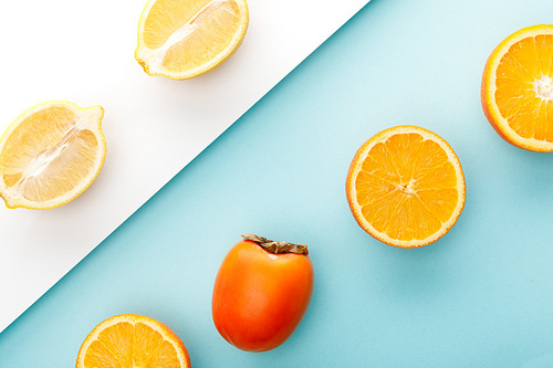 Top view of orange and lemon halves with persimmon on blue and white background