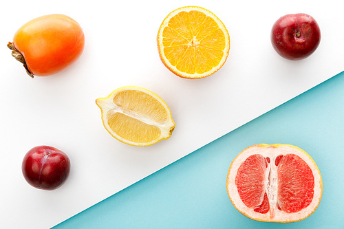 Top view of orange, lemon and grapefruit halves with persimmon, apples on white and blue background