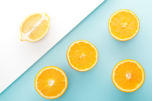 Top view of cut oranges and lemon half on white and blue background