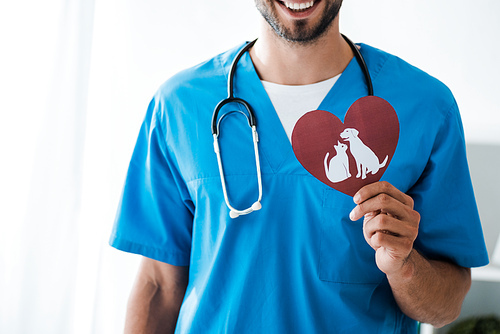 cropped view of smiling veterinarian showing paper cut heart with dog and cat symbols