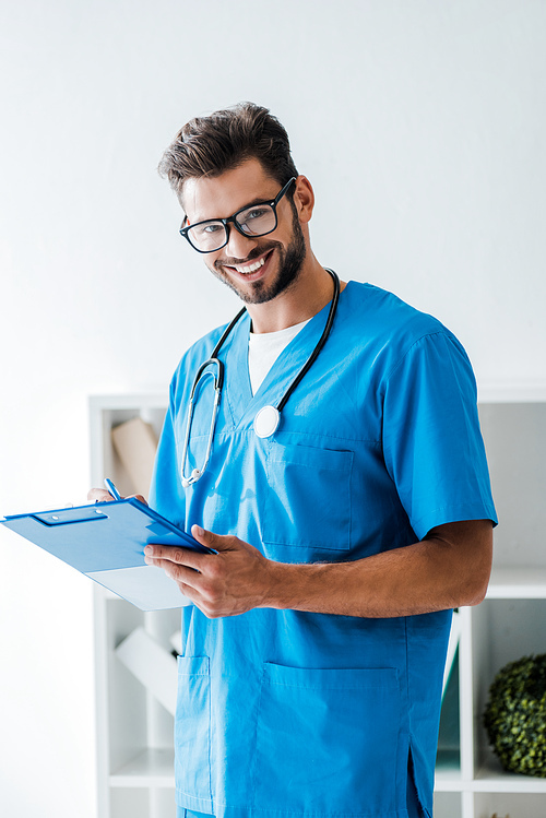 handsome veterinarian smiling at camera while writing prescription on clipboard