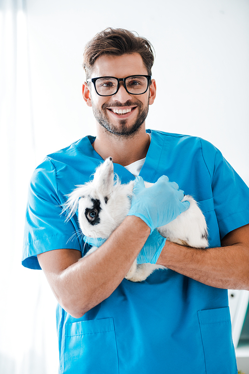 handsome veterinarian smiling at camera while holding cute black and white rabbit on hands