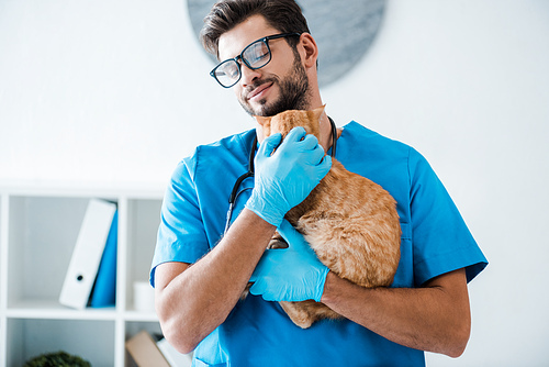 young, smiling veterinarian holding cute red cat on hands