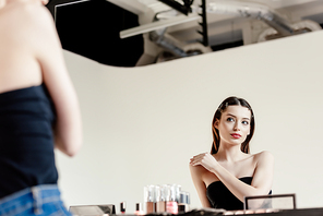 selective focus of beautiful model looking at mirror in photo studio