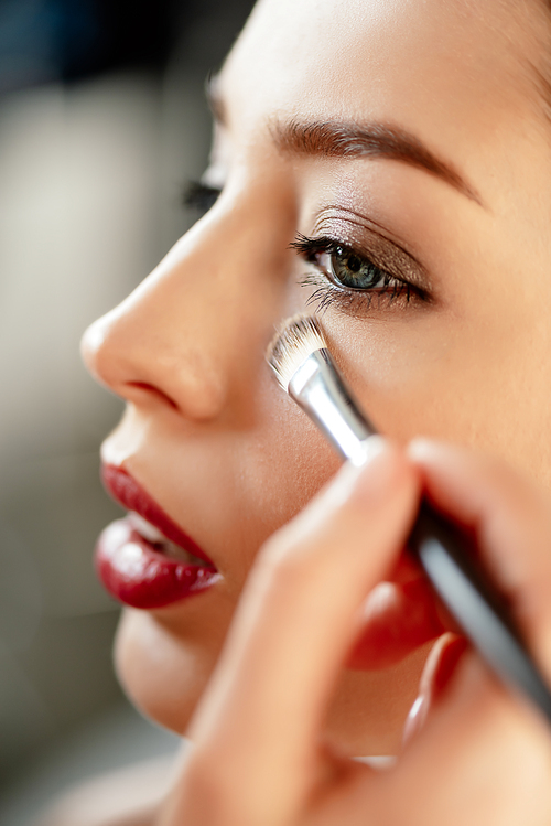 selective focus of makeup artist applying concealer on model