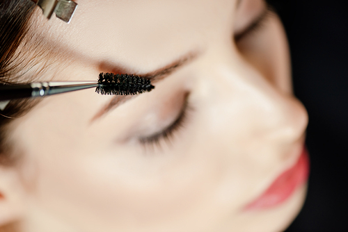 selective focus of eyebrow brush near woman with closed eyes