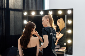 woman in black t-shirt with makeup artist lettering applying decorative cosmetics on model