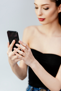 selective focus of woman using smartphone isolated on grey