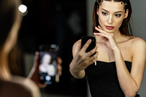 selective focus of attractive woman taking selfie in photo studio