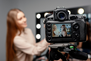 selective focus of digital camera with happy makeup artist applying face powder on beautiful model